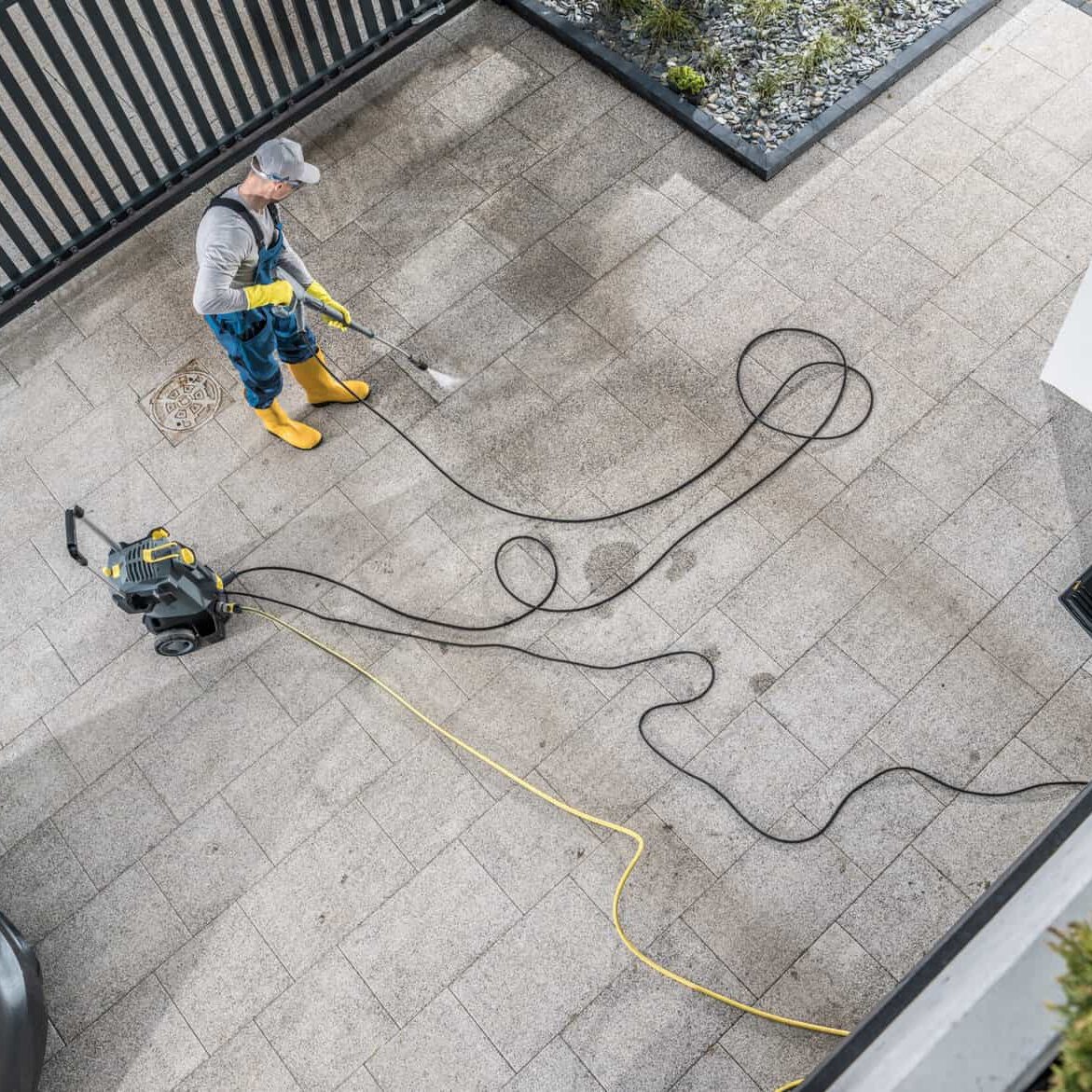 Caucasian Home Owner Pressure Washing His Dirty Driveway Aerial Photo. Keeping Concrete Driveway Bricks Clean.
